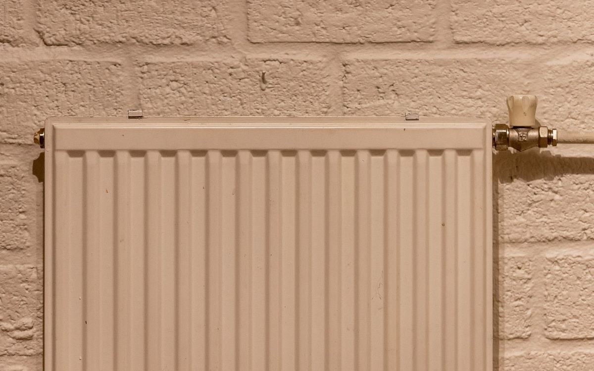 White panel radiator with a valve on a painted brick wall